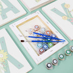 Art supplies including paint tubes and brushes on a light green surface with framed artworks.