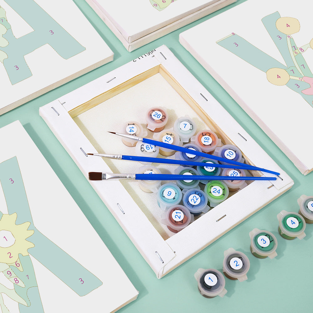 Art supplies including paint tubes and brushes on a light green surface with framed artworks.