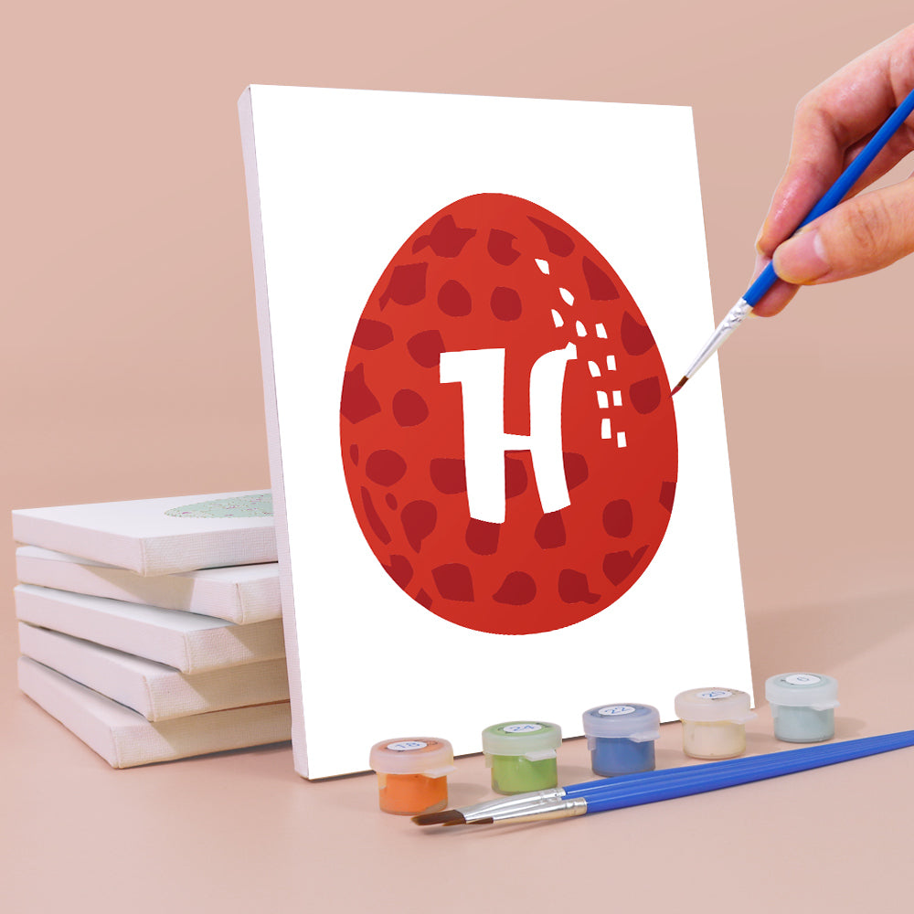 Person malt ein rotes Ei mit einem weißen Buchstaben „H“ auf einer weißen Leinwand, mit Farbbehältern und Pinseln auf beigem Hintergrund.