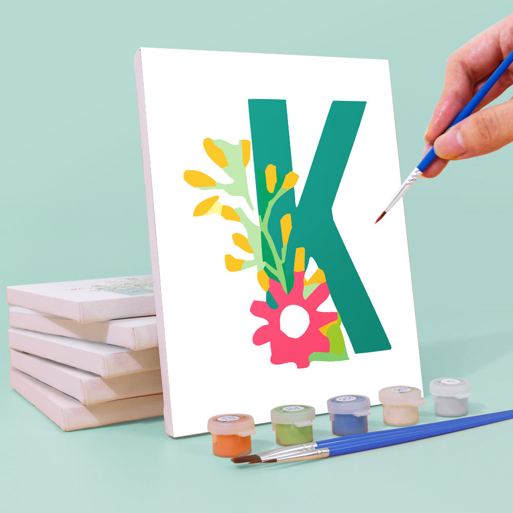 Hand painting a colorful letter 'K' on a canvas with paint supplies.