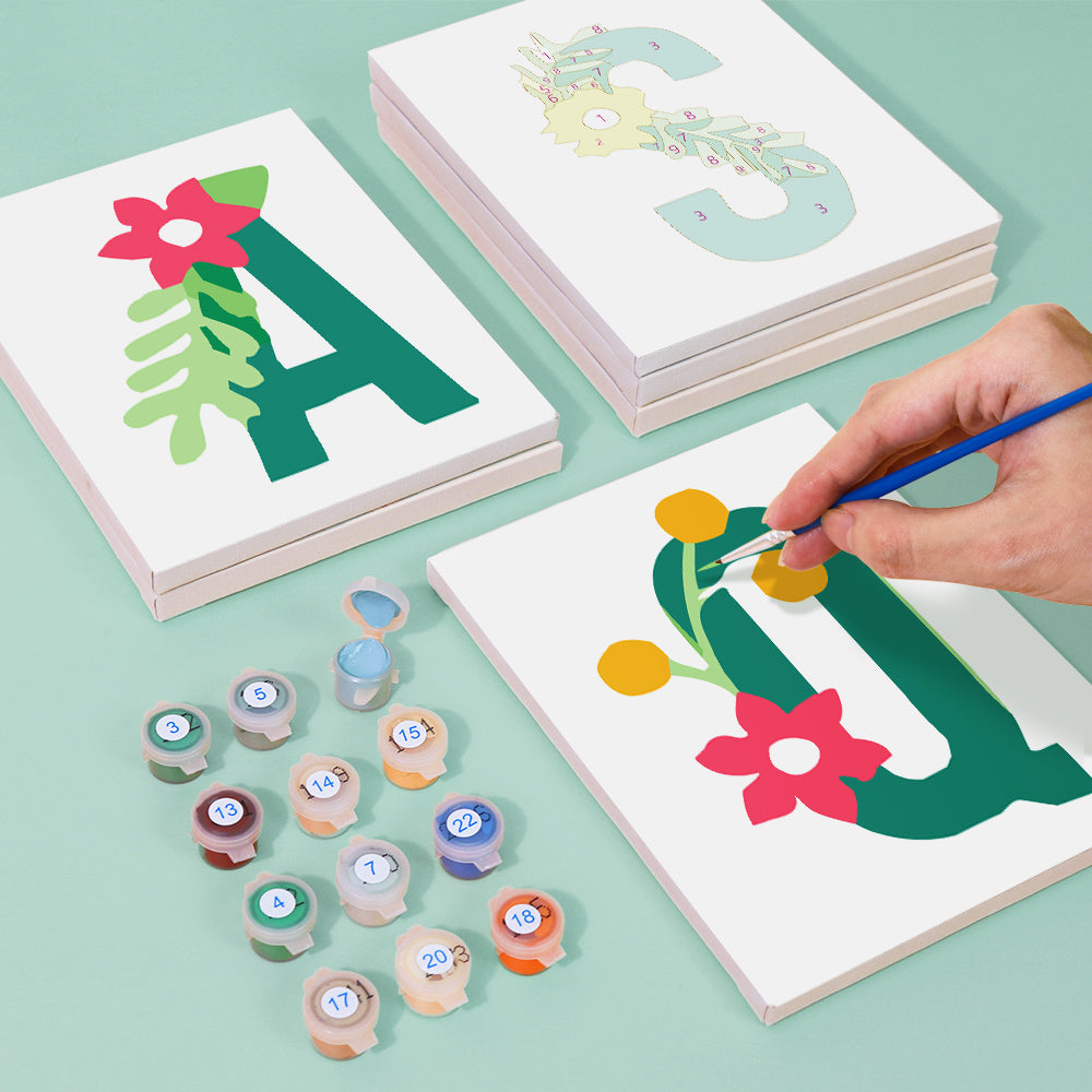 Children's art project with letter 'A' designs and paint pots on a light green background