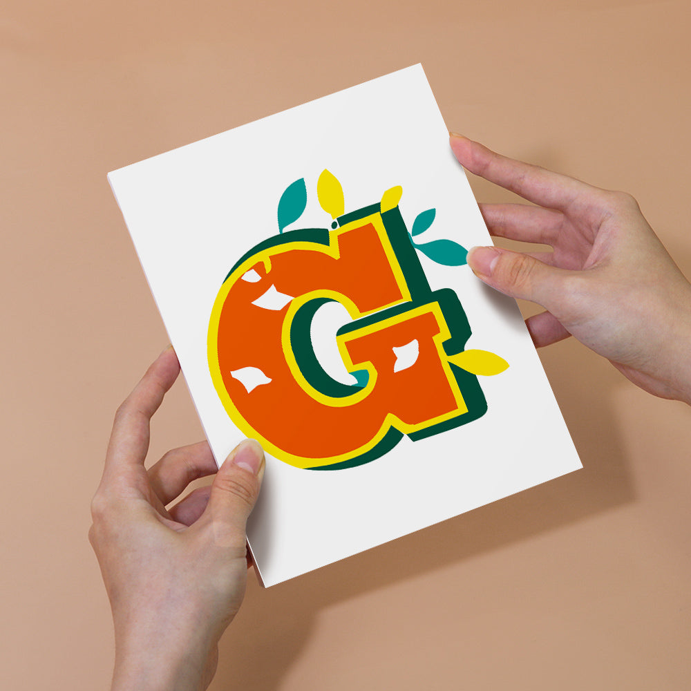 Colorful letter 'G' design on a white card held by hands against a beige background