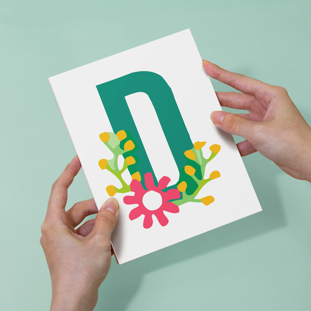Card with letter 'D' and floral design held by hands against a light green background