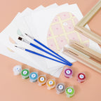 Art supplies including paintbrushes, color swatches, and a small easel on a peach background