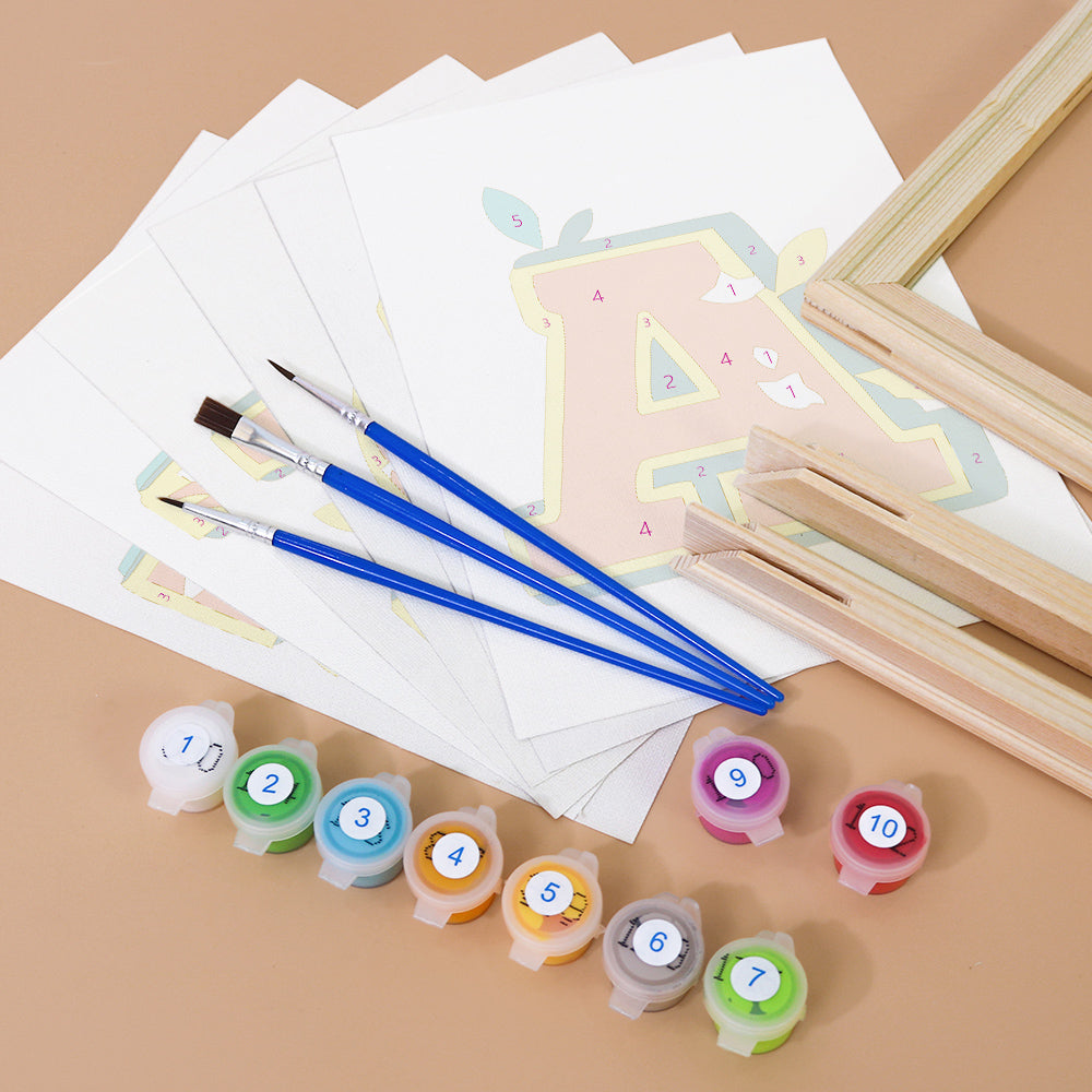 Art supplies including paintbrushes, paint containers, and paper with letter 'A' designs on a brown background.
