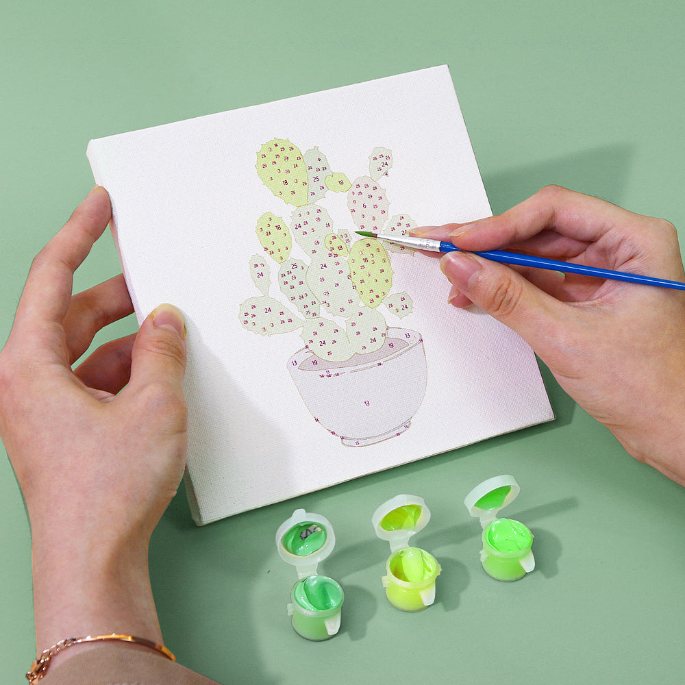Set of tiny paint pots arranged next to a leafy plant canvas