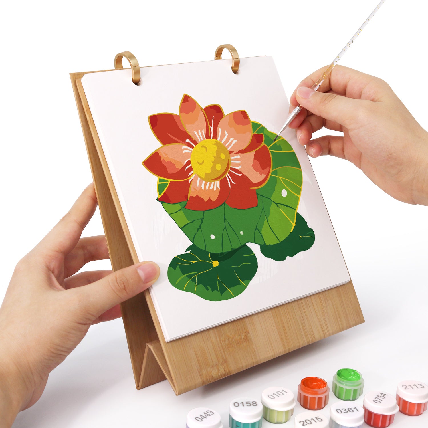 Hand holding a small easel with a colorful flower painting on a white background