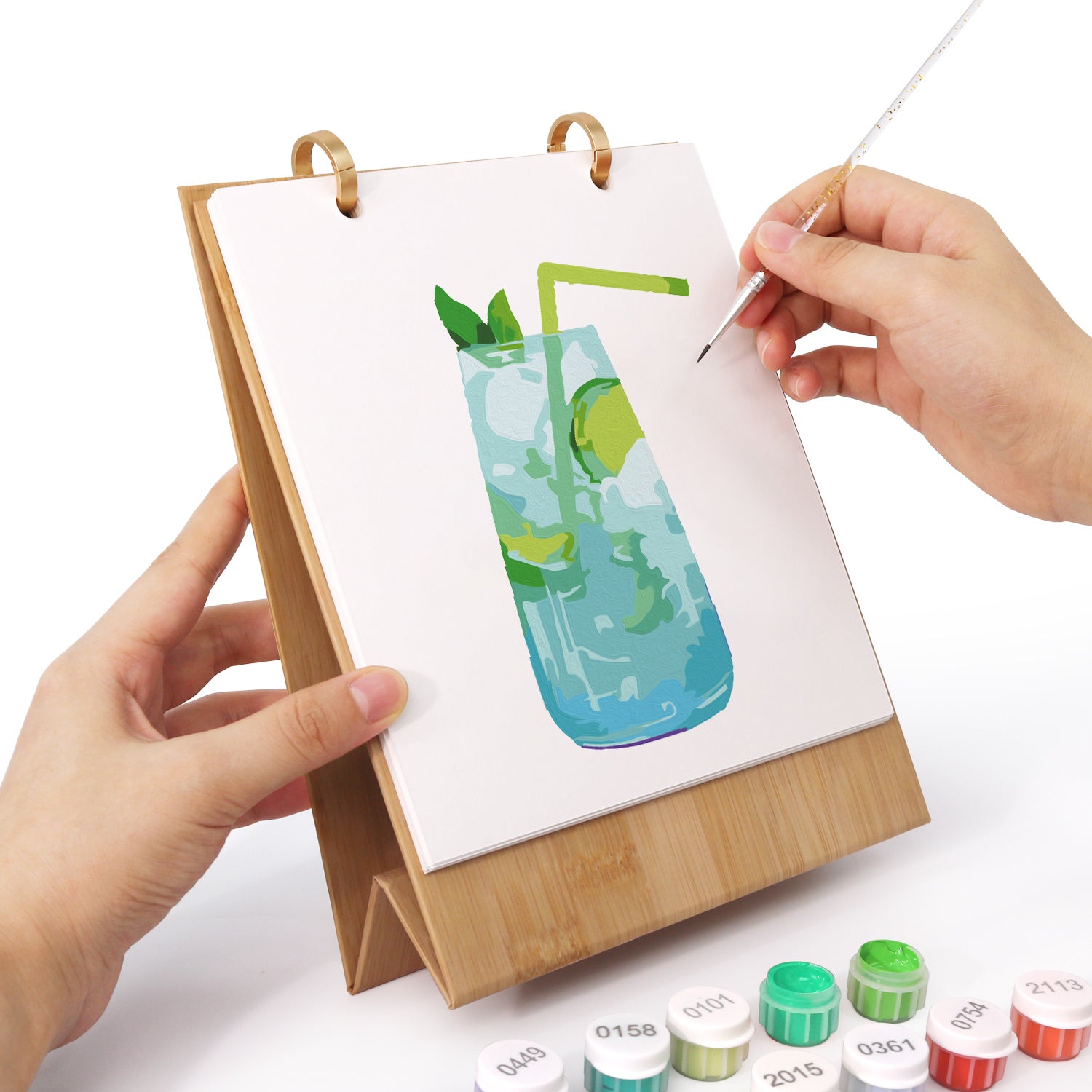 Person painting a glass of water with mint leaves on a small easel with paint supplies.