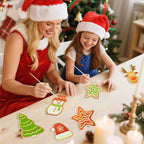 Woman and child wearing Santa hats decorating Christmas cookies with a decorated tree in the background.