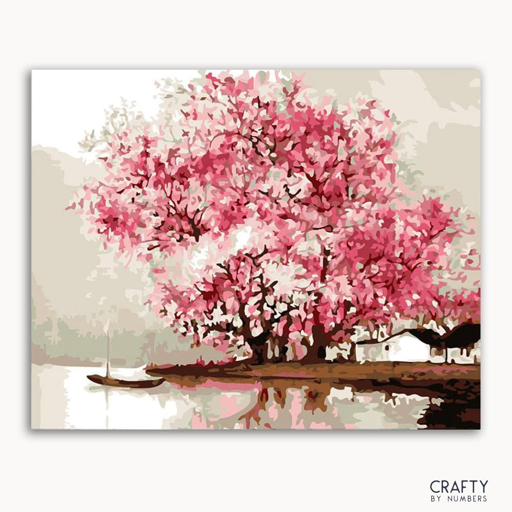 A paint-by-numbers kit depicting a cherry blossom tree with soft pink shades, surrounded by a body of water with a boat in the distance.