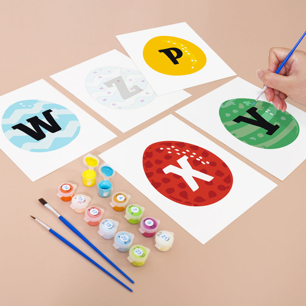 Children's painting activity with alphabet letters on paper and paint supplies.