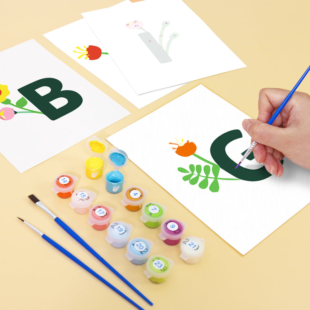 Children's art project with letters 'B' and 'G', paint containers, and brushes on a yellow surface.