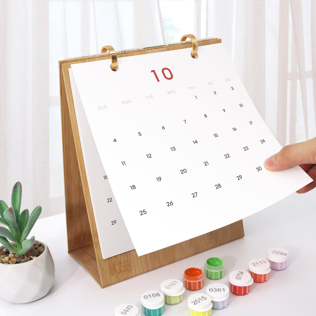 Calendar with a wooden stand on a white surface with small containers and a plant.