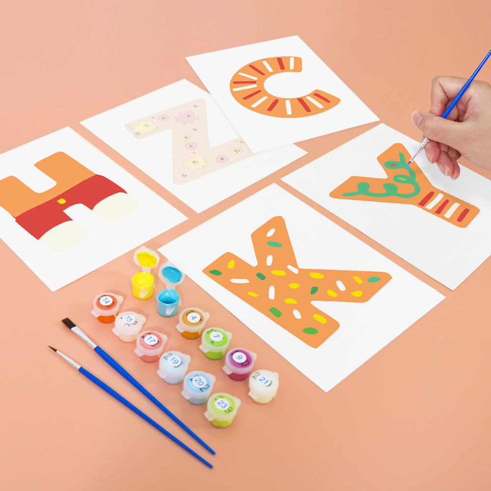 Children's art project with painted letters on paper and art supplies on a peach-colored background