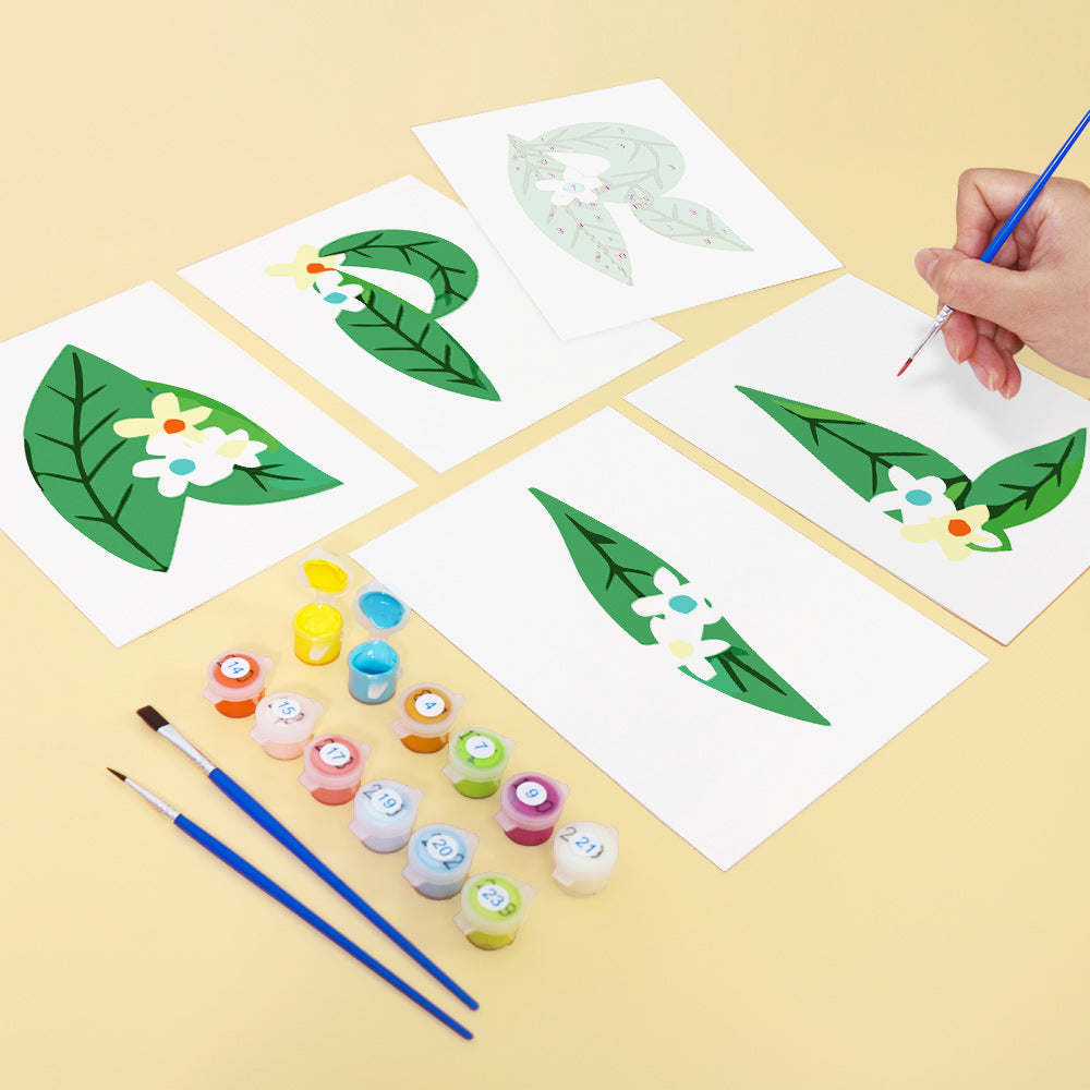 Children's painting activity with leaf and flower designs on paper, paint bottles, and brushes on a yellow background.