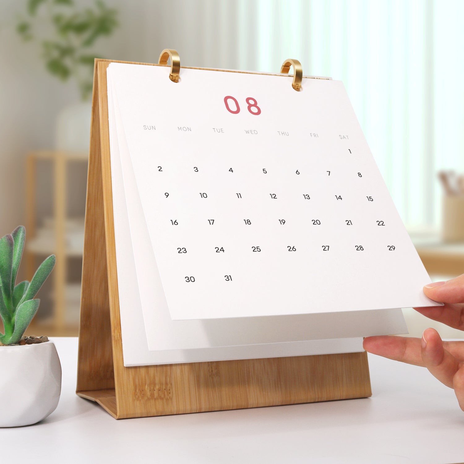 Calendar with wooden stand on a table, with a hand adjusting the page.