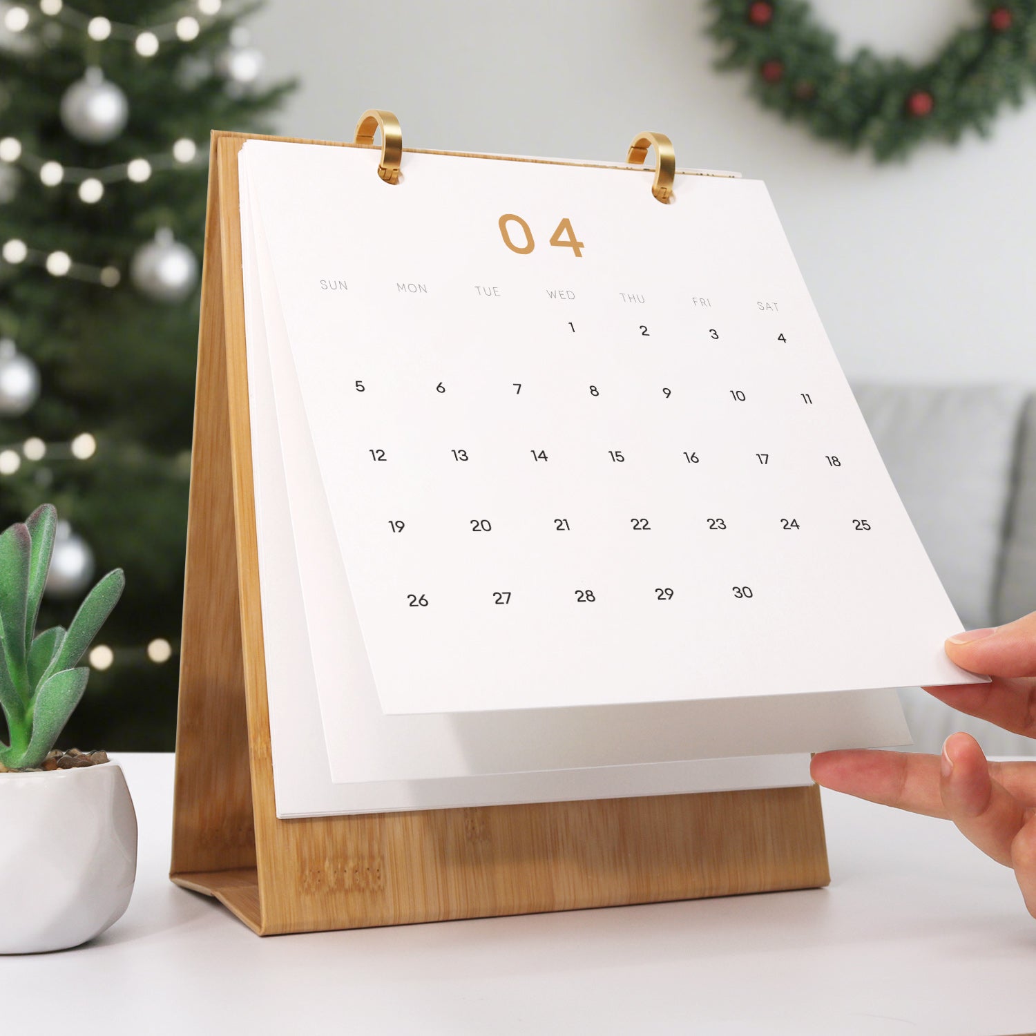 Calendario con soporte de madera sobre una mesa, adornos navideños al fondo