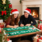 Two people wearing Santa hats decorating a Christmas banner in front of a fireplace.