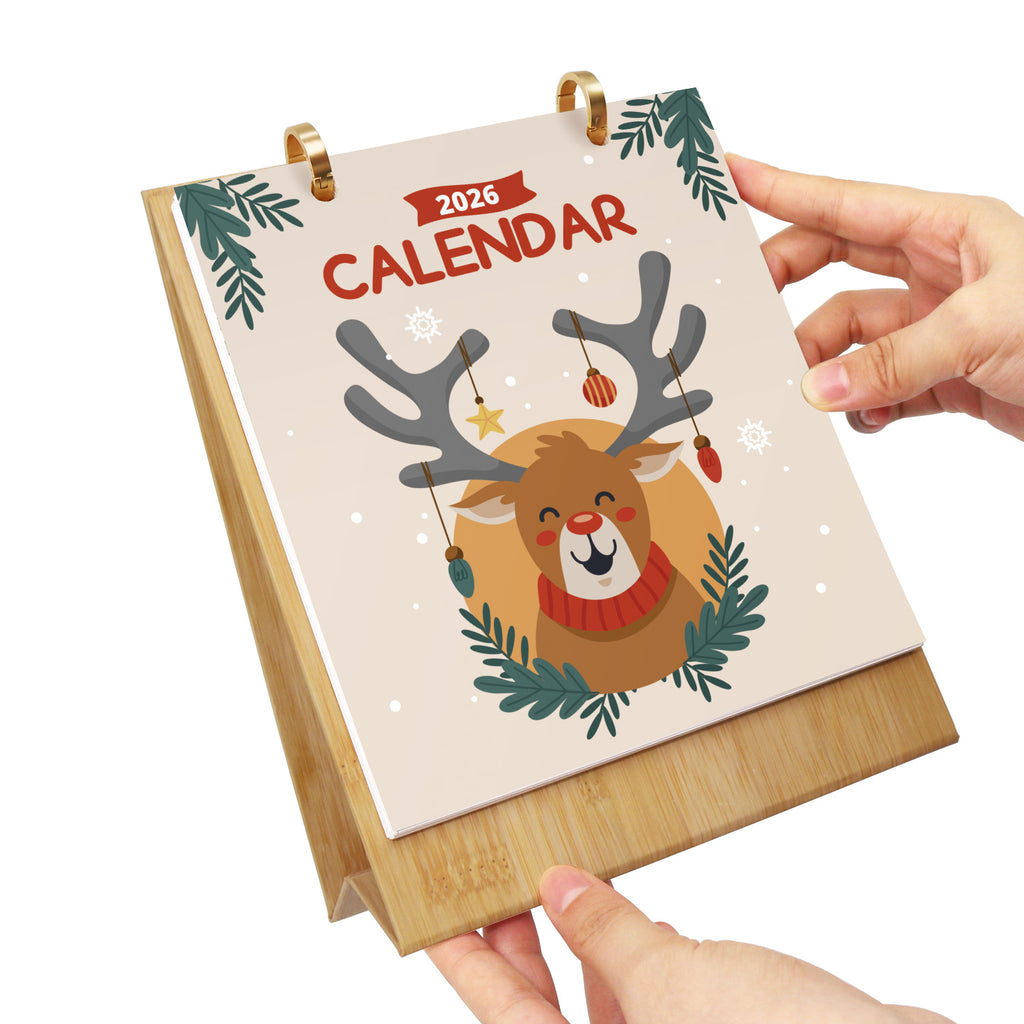 Calendario con un diseño de renos sostenido por una mano sobre un fondo blanco.