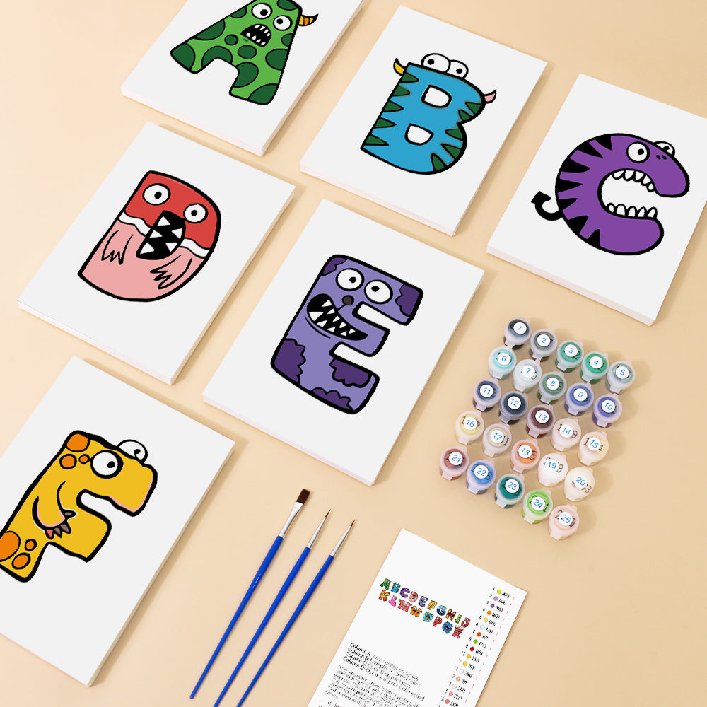 Colorful alphabet cards with monster designs on a beige surface, accompanied by paint bottles and brushes.