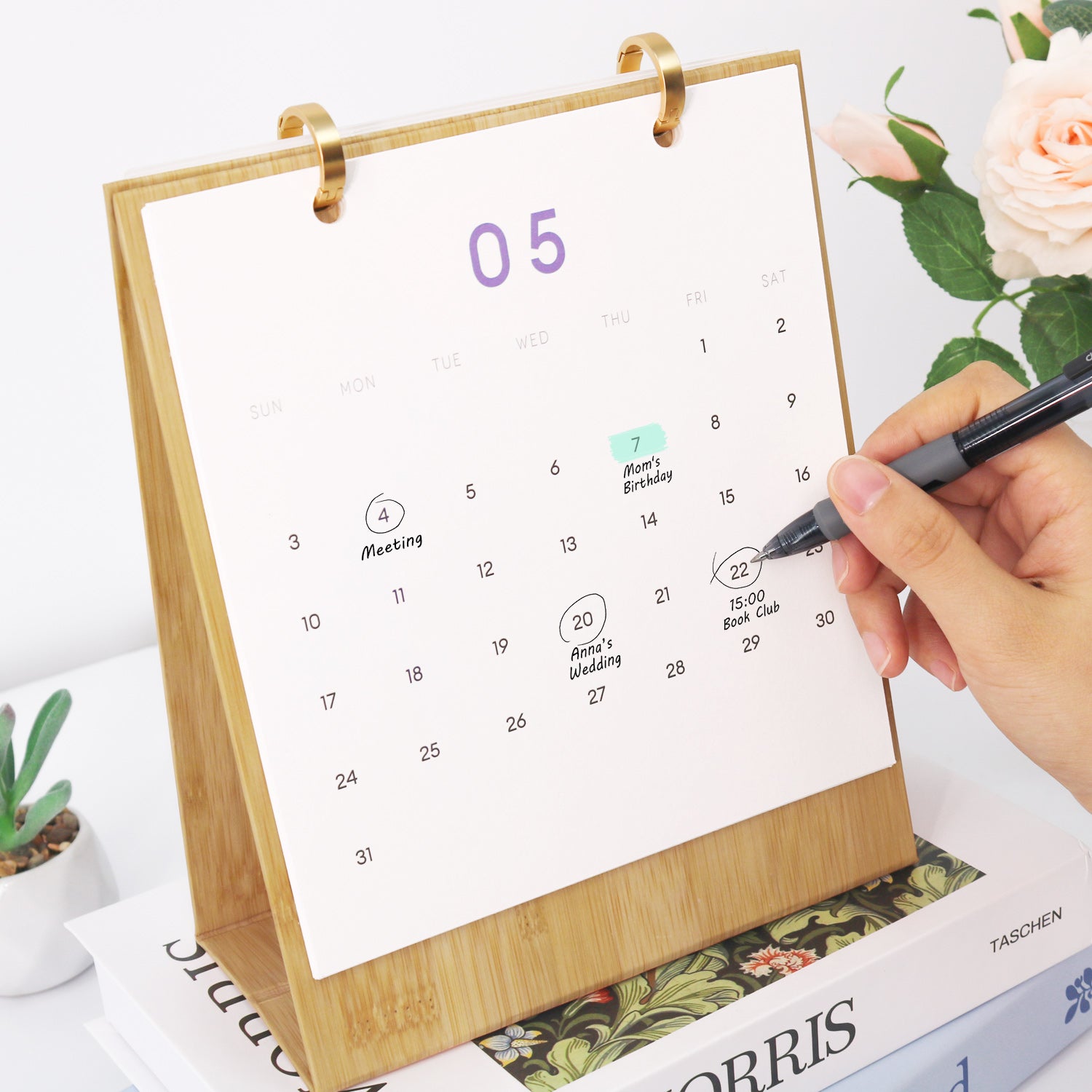 Desk calendar with a hand holding a pen, set against a floral background
