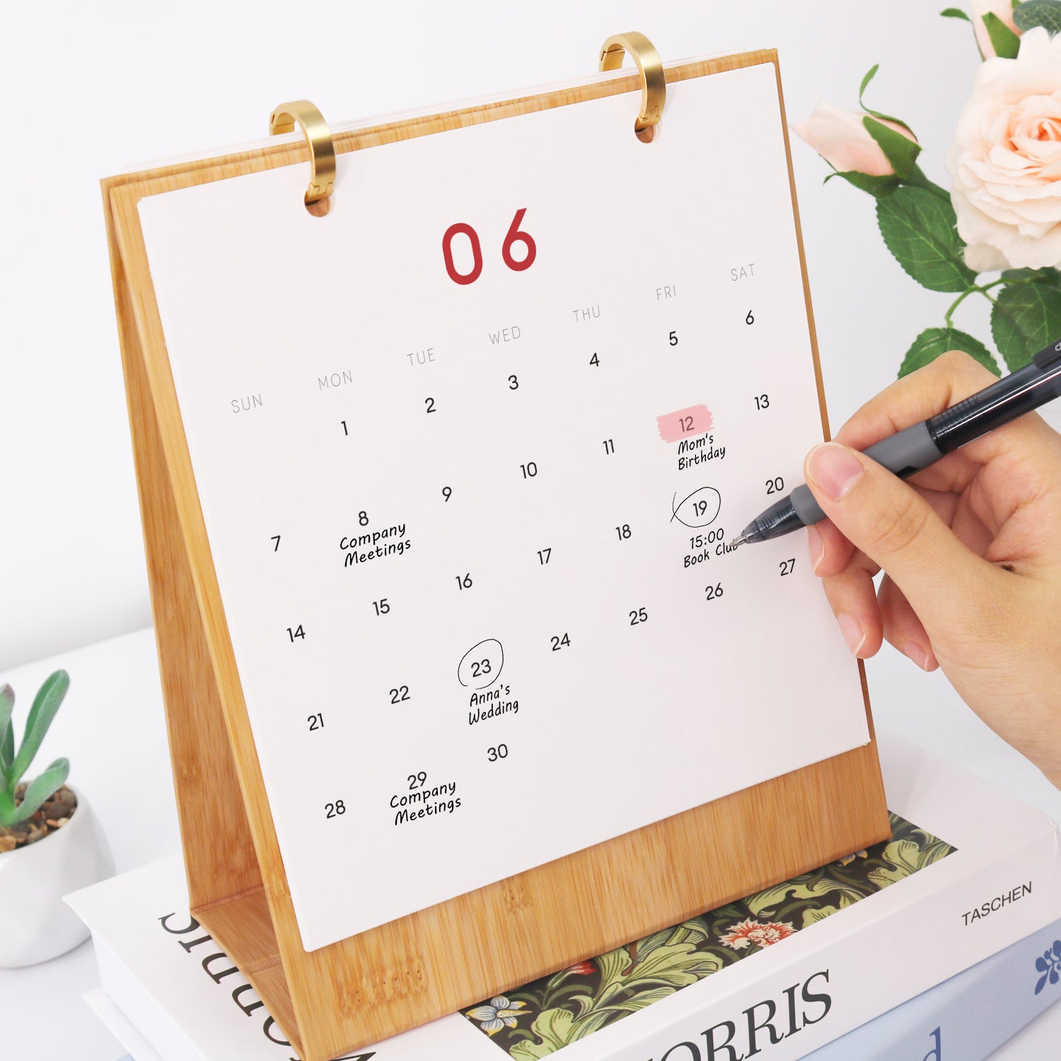 Person, die mit einem Stift ein Datum auf einem Kalender markiert und auf einer Zeitschrift mit floralen Elementen platziert ist.