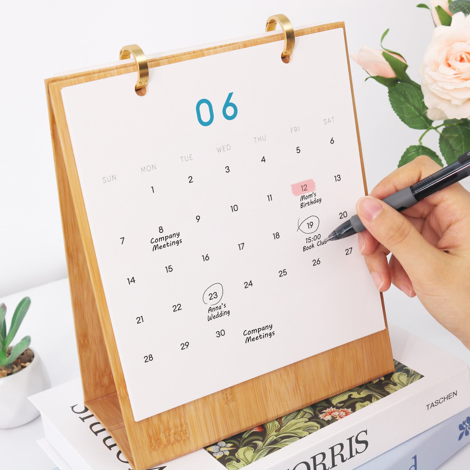 Person, die mit einem Stift ein Datum auf einem Kalender markiert und auf einer Zeitschrift mit floralen Elementen platziert ist.