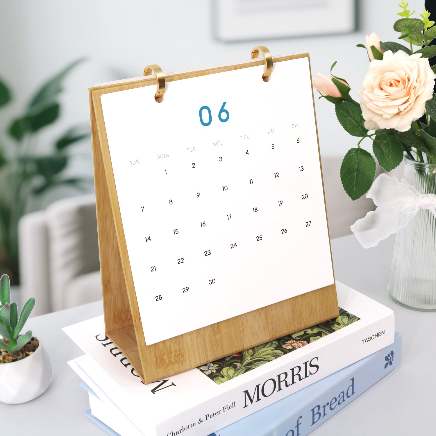 Tabletop calendar on a stack of books with a vase of flowers in the background