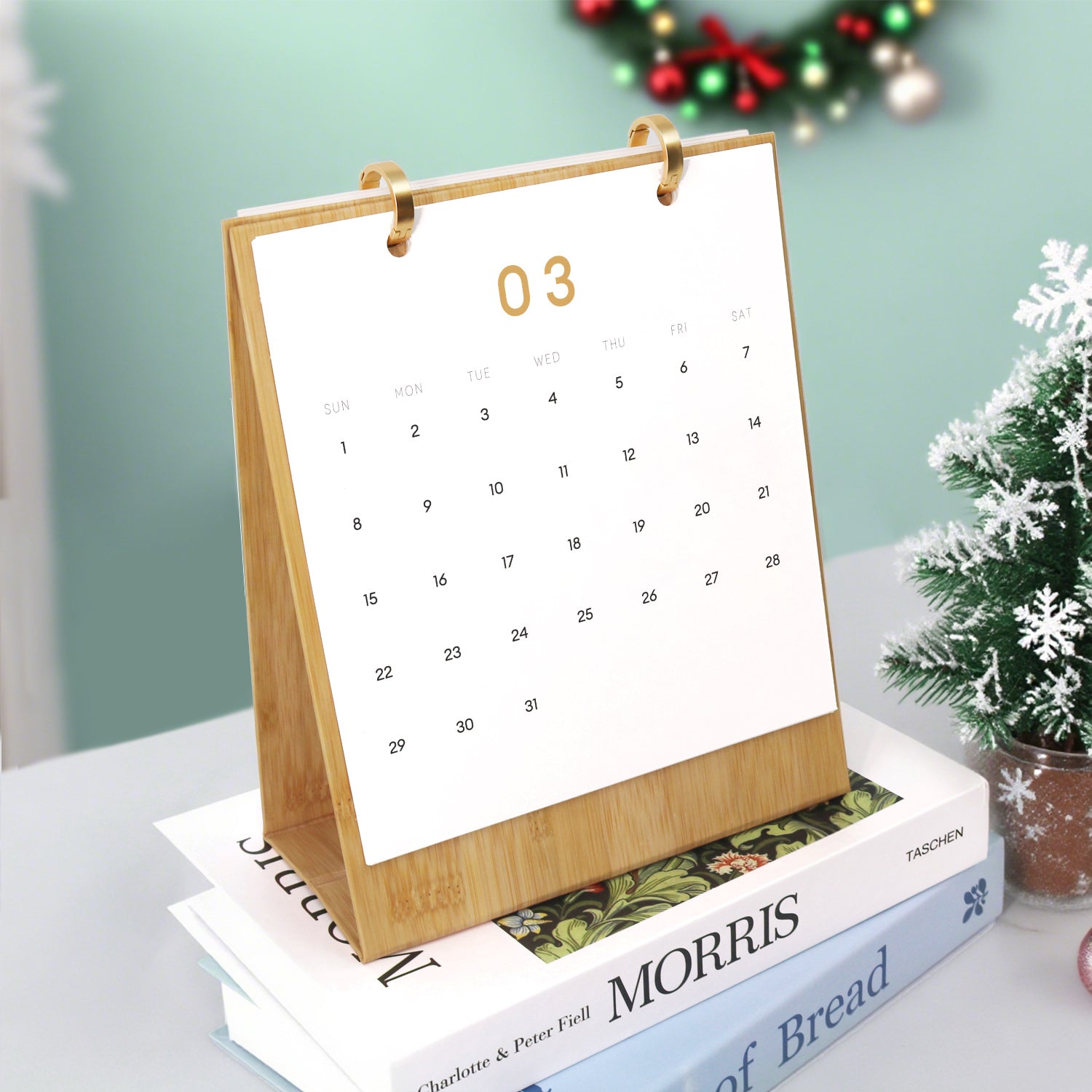 Calendar with a wooden stand on top of books, with a Christmas wreath in the background.