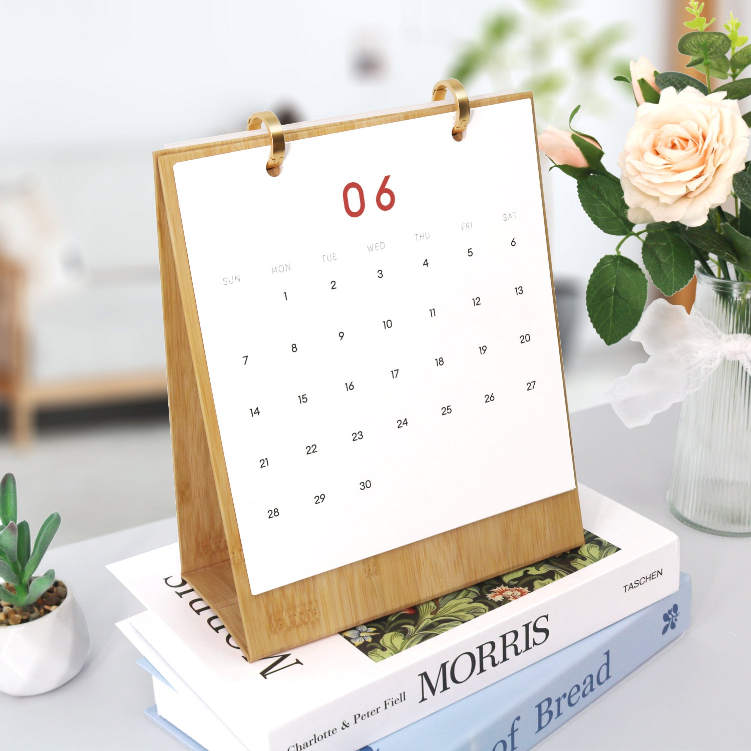 Tabletop calendar on a stack of books with a vase of flowers in the background