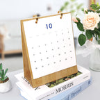 Calendar on a wooden stand with a vase of flowers and books in the background