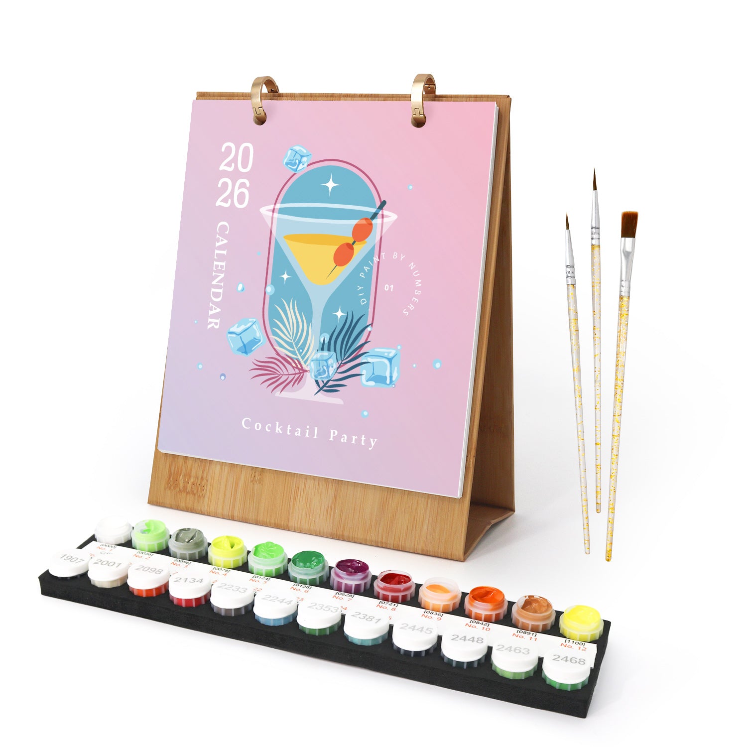 Desk calendar with cocktail design, paintbrushes, and paint tubes on a white background