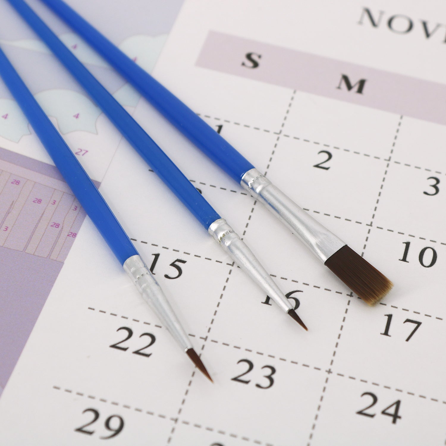 Three paintbrushes on a calendar page with dates visible