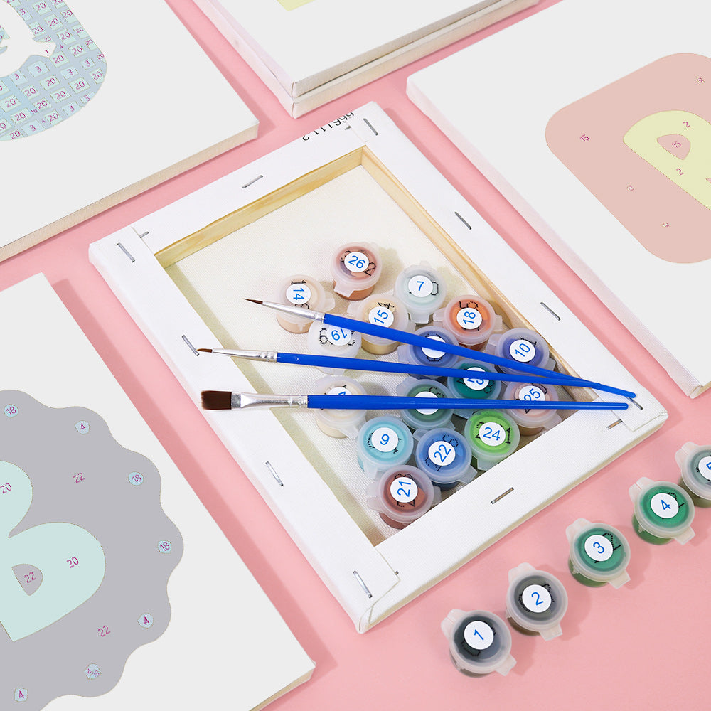 Set of paint tubes and brushes on a pink surface with a framed picture in the background