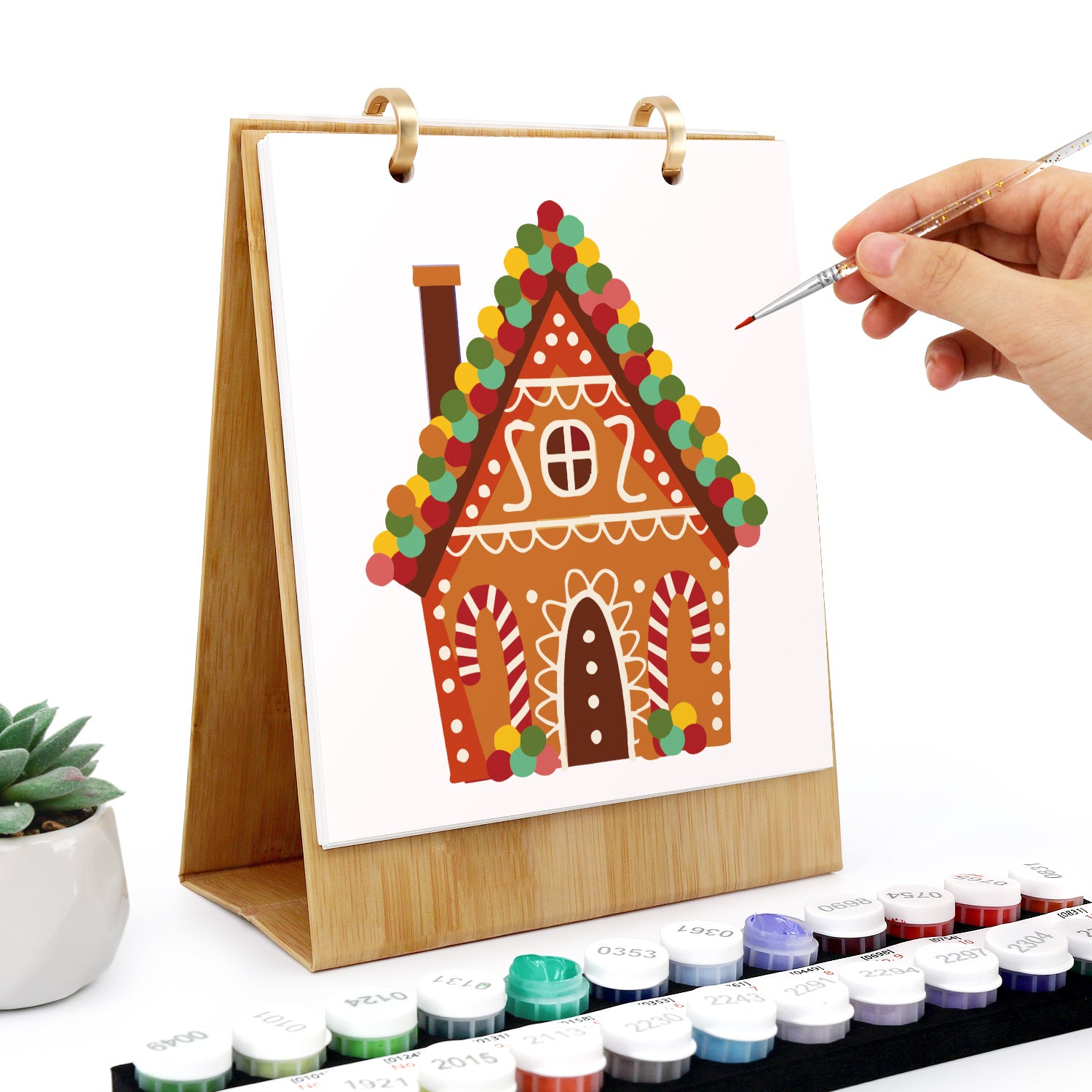Hand painting a gingerbread house illustration on a canvas with watercolors.