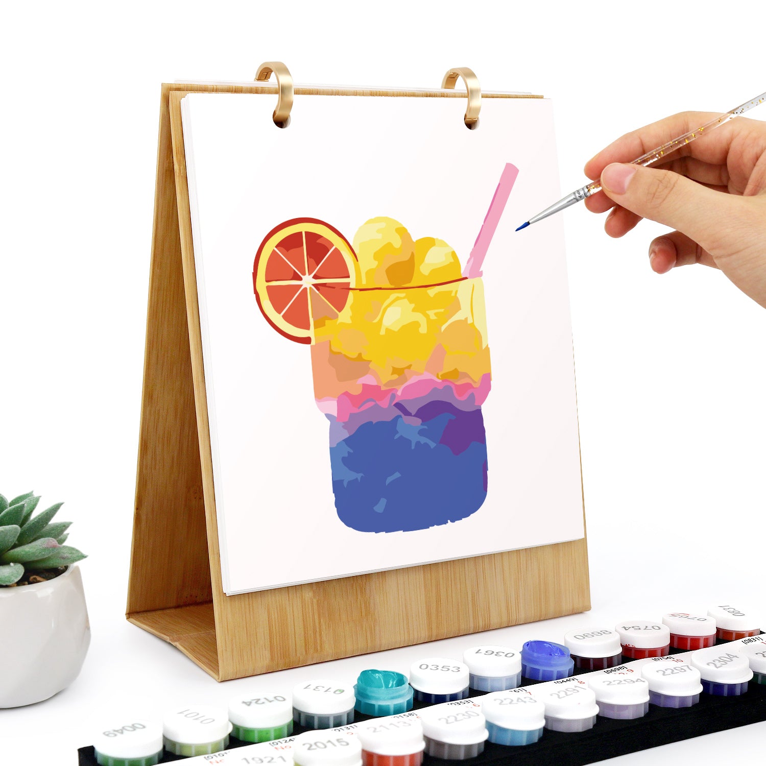 Person malt eine bunte Getränkeillustration auf einer kleinen Staffelei mit Wasserfarben.