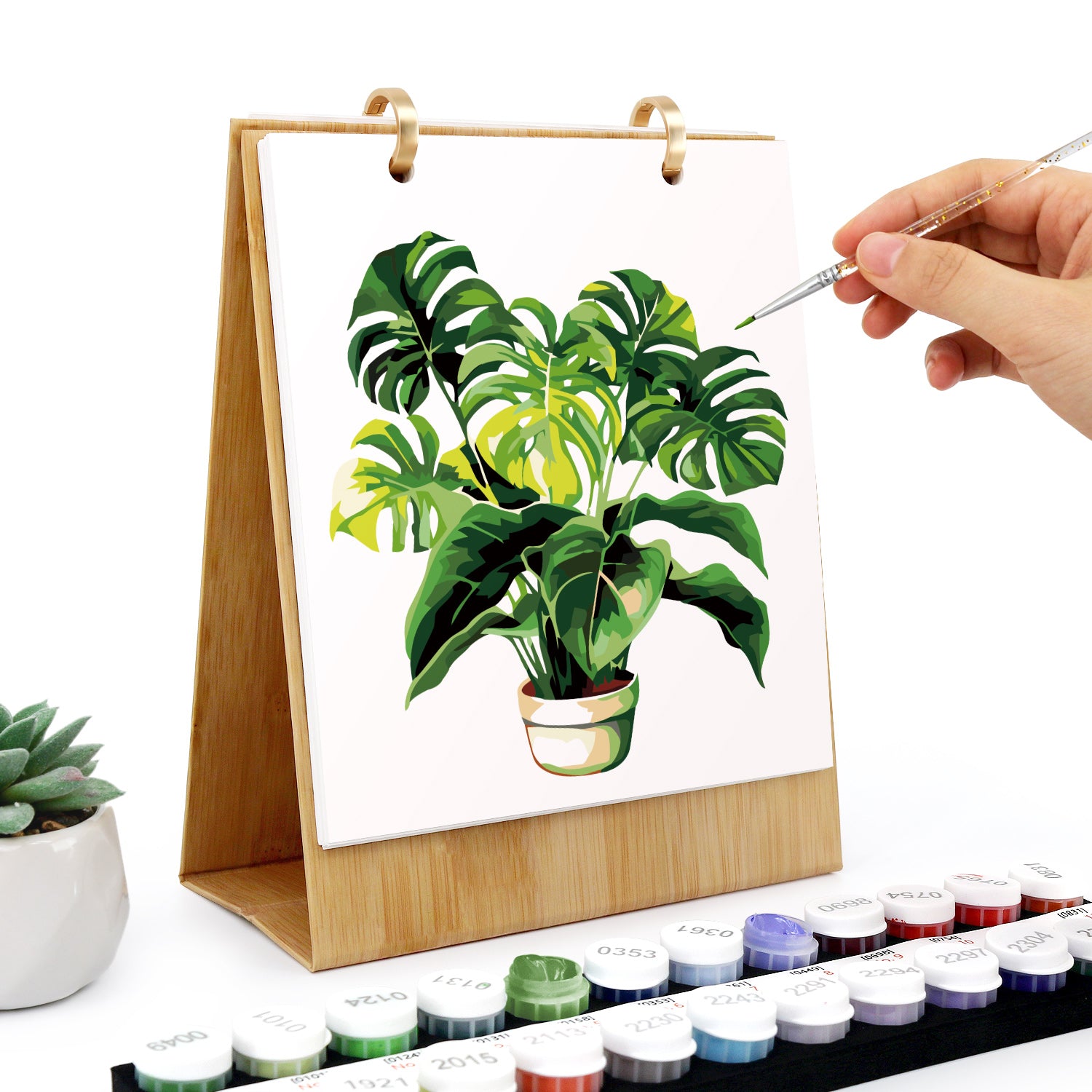 Persona pintando una planta en un pequeño lienzo con acuarelas.