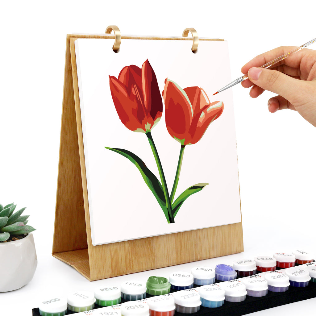 Person painting red tulips on a small canvas with watercolor paints.