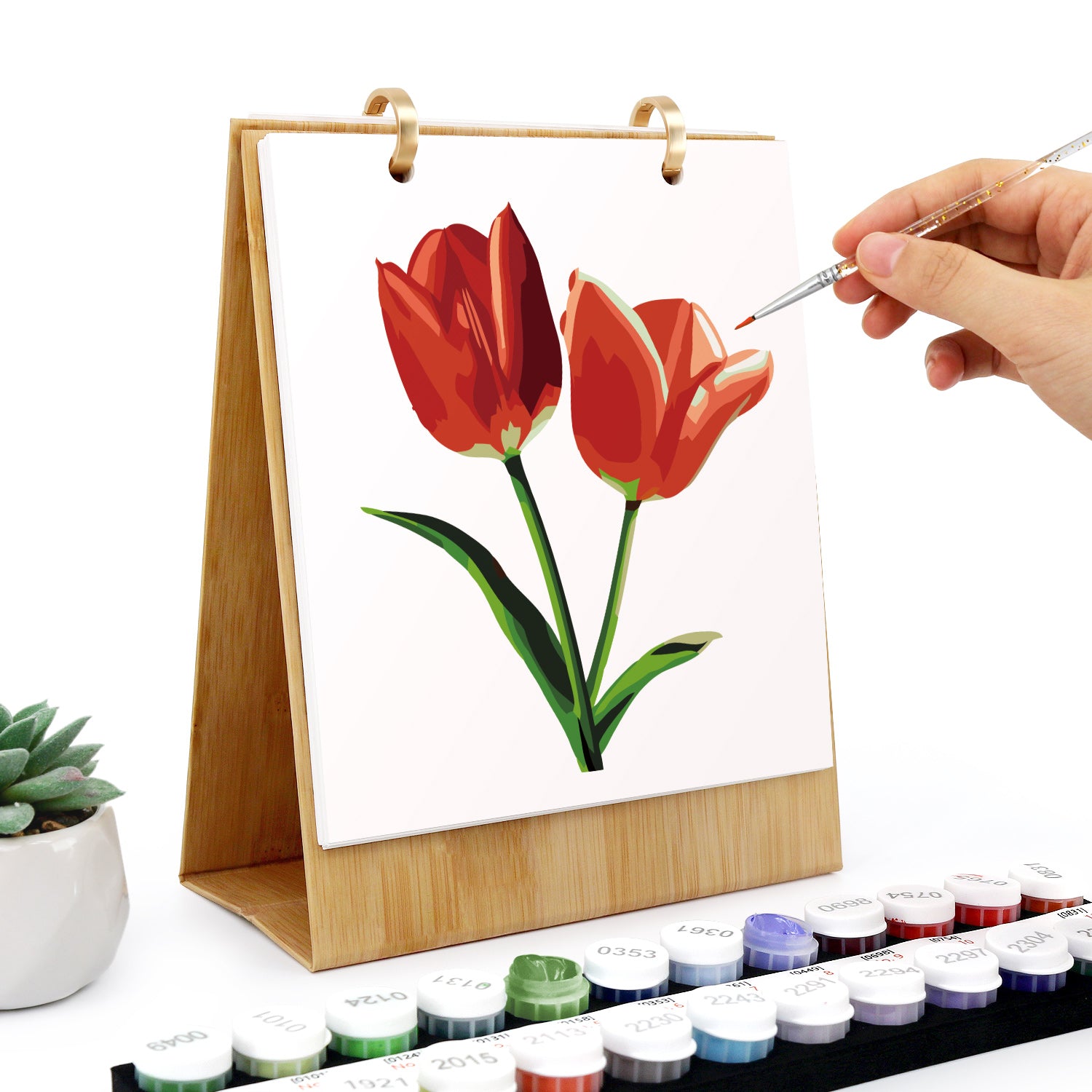 Person painting red tulips on a small canvas with watercolor paints.
