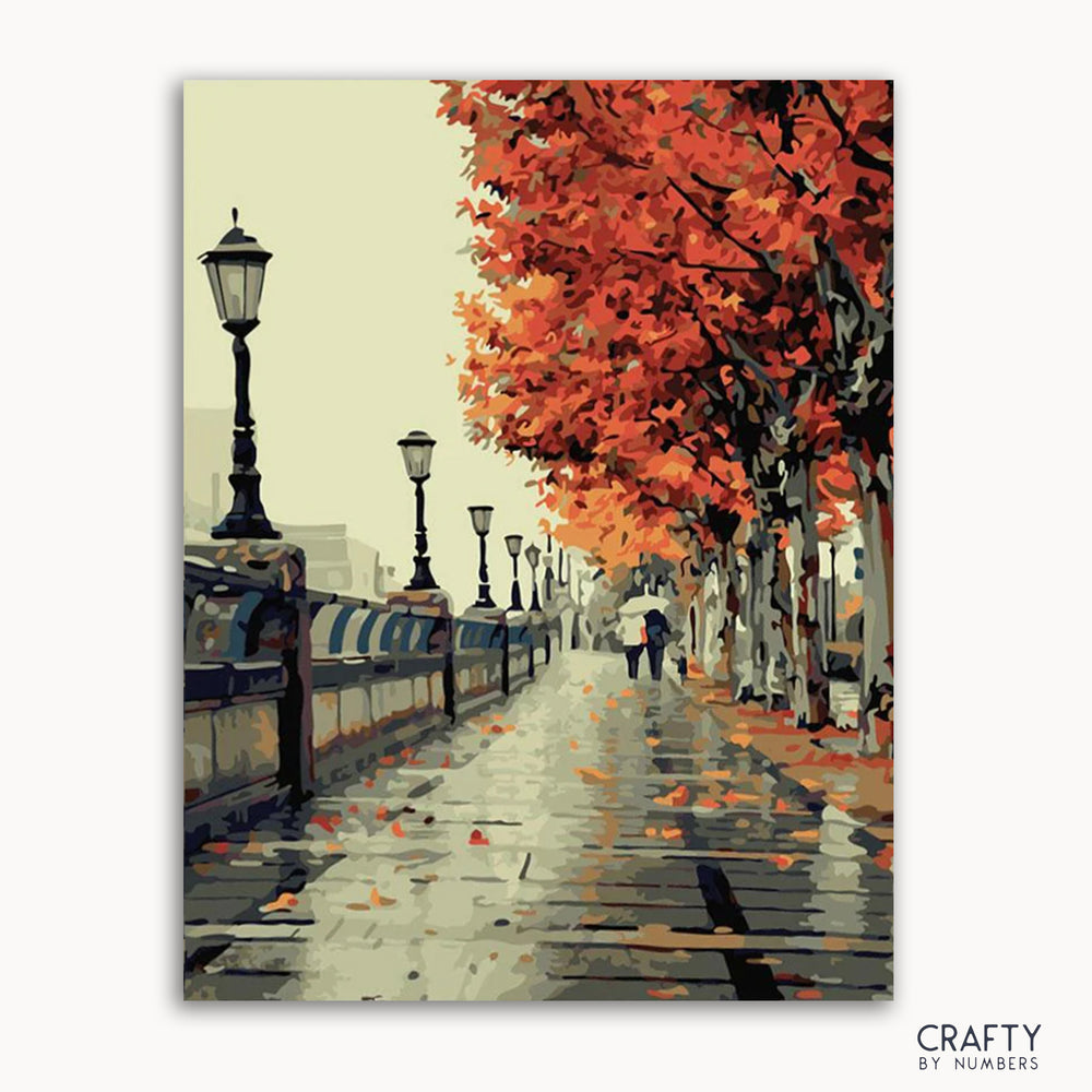 A paint-by-numbers kit depicting a autumnal street scene with trees, a person walking, and street lamps.
