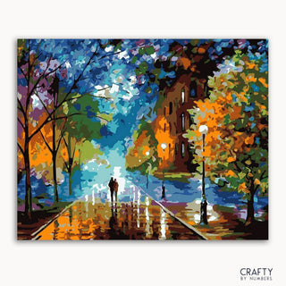 Un lienzo con una pintura de una escena de una calle lluviosa con una pareja caminando, árboles al costado y un edificio al fondo, con la etiqueta 'CRAFTY BY NUMBERS'.