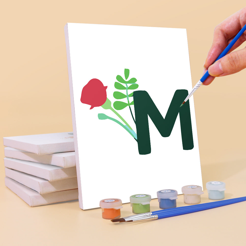 Hand painting a letter 'M' with flowers on a canvas, surrounded by paint cans and brushes.