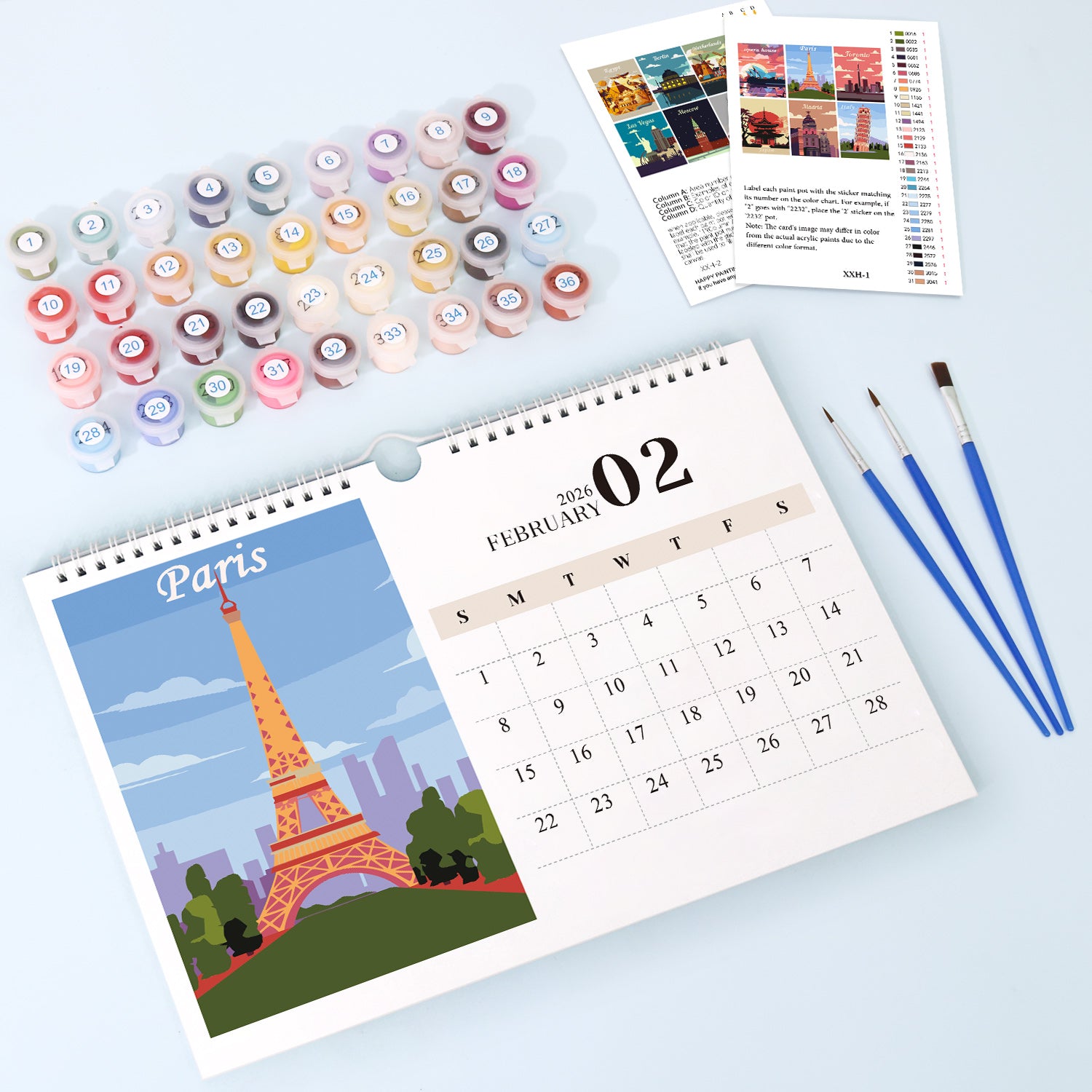 Calendar with Eiffel Tower design, paint bottles, and brushes on a light blue background