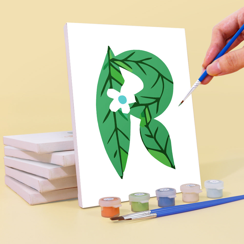 Hand painting a green leafy design on a white canvas with paint supplies.