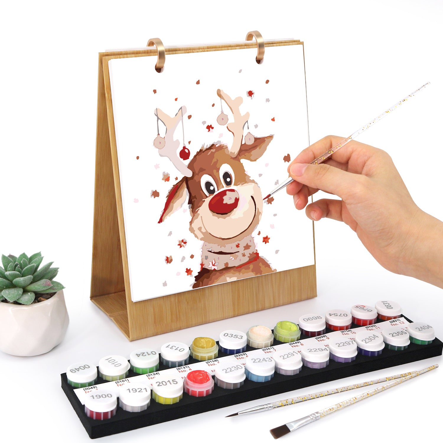 Hand painting a reindeer illustration on a watercolor card with paint set and tools on a white background
