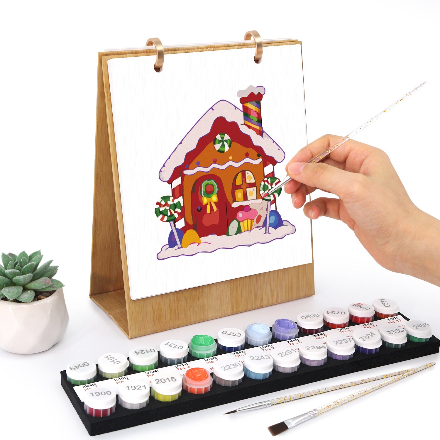 Hand painting a gingerbread house on a transparent canvas with watercolor paints and brushes.