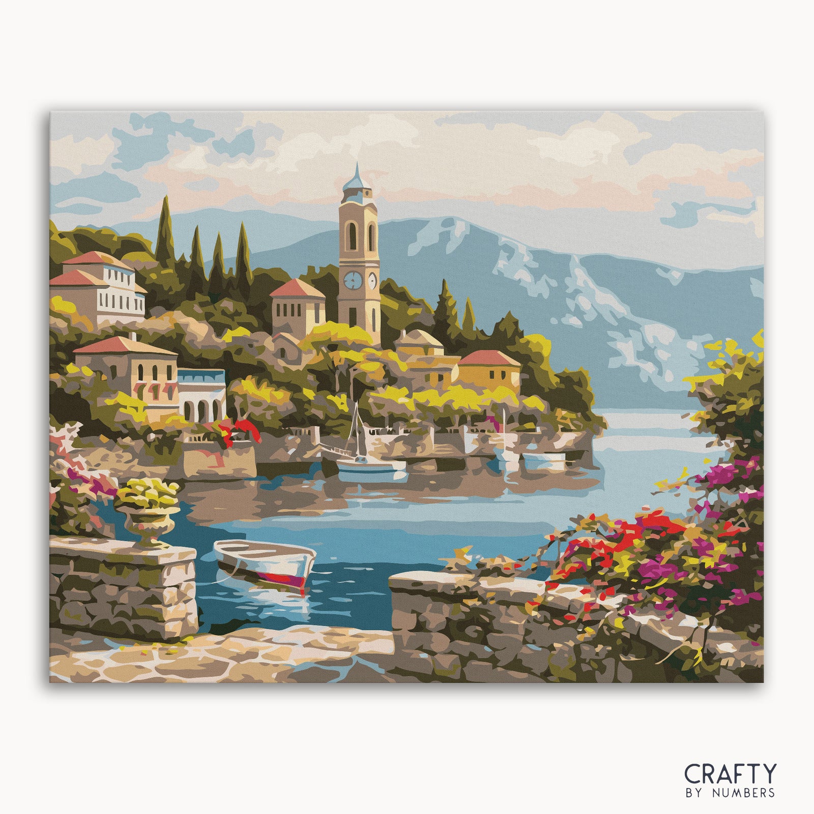 Un kit de pintura que representa un pueblo sereno junto a un lago con montañas al fondo, casas, un barco y una torre de reloj, titulado "Pueblo del Lago Como".
