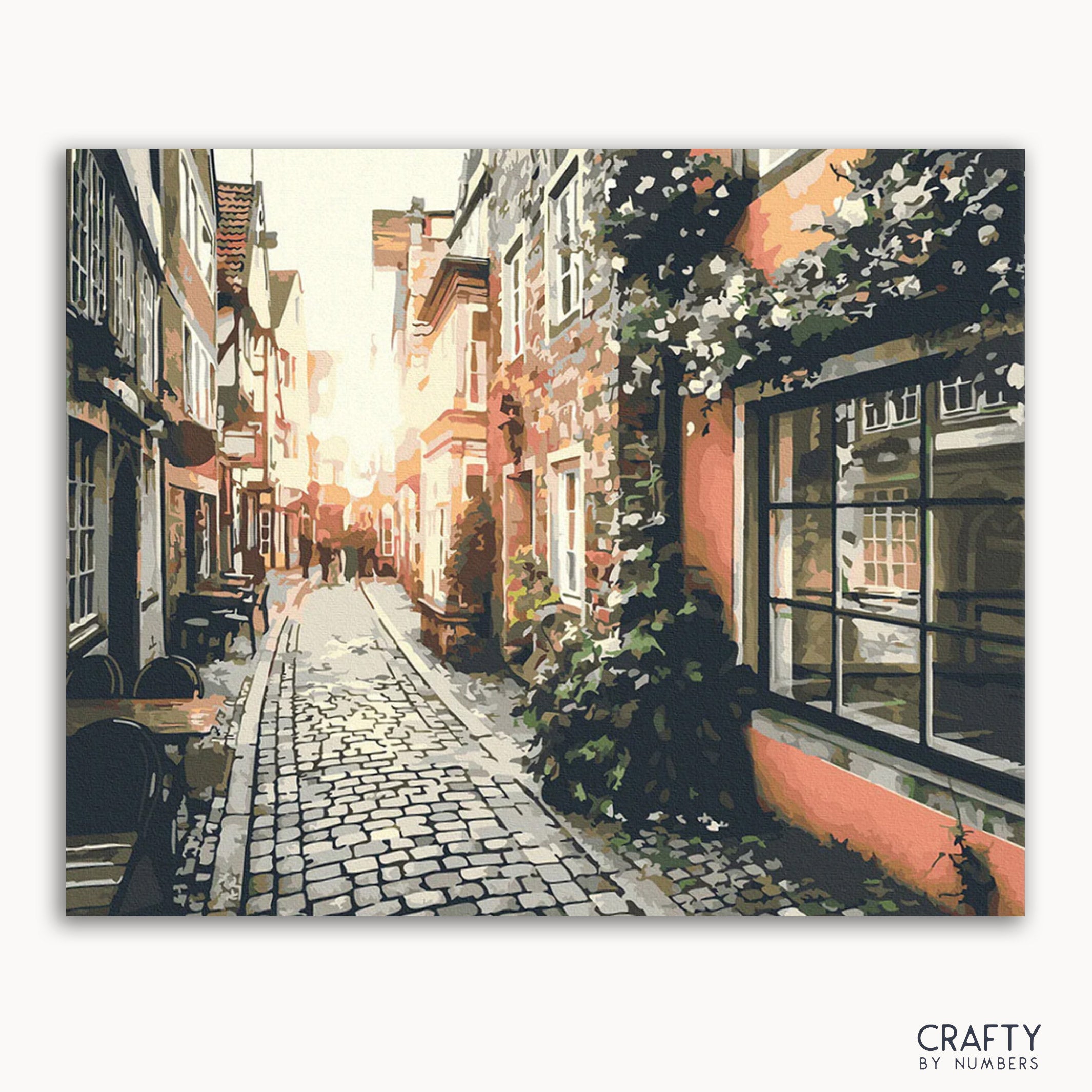 A canvas painting depicting a quiet street in an old town at sunset, with cobblestone pavement, buildings on either side, and hanging flowers.