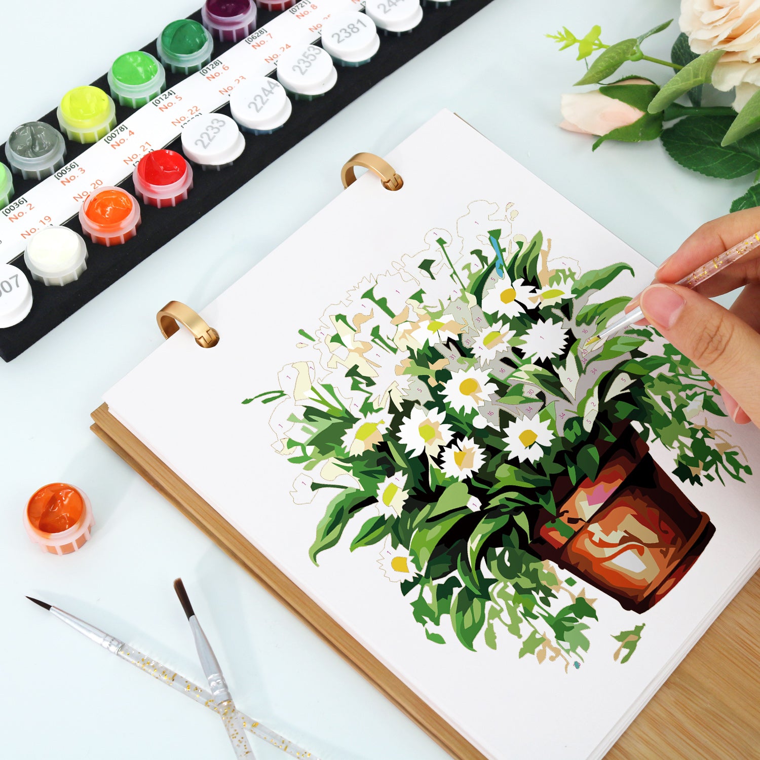 Persona pintando una escena floral sobre un lienzo con acuarelas.