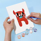 Person painting a red cartoonish creature on a white canvas with paint containers below.